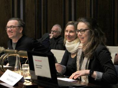Vier Personen sitzen nebeneinander hinter Pulten im Hodlersaal des Neuen Rathauses und lachen.