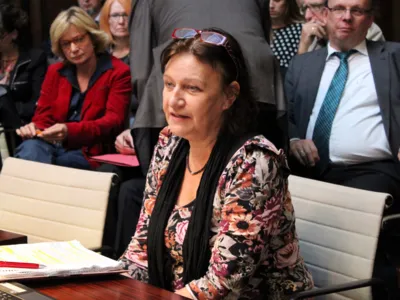 Eine Frau sitzt im Hodlersaal und spricht. Dabei tr&auml;gt sie ihre Brille &uuml;ber der Stirn. Hinter ihr sind ca. acht weitere Personen erkennbar.