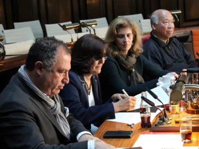 Vier personen sitzen im Hodlersaal nebeneinander hinter Pulten. Eine davon schreibt etwas auf ein papier. das vor ihr liegt.