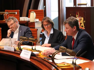 Drei Personen sitzen im Hodlersaal hinter Pulten. 
