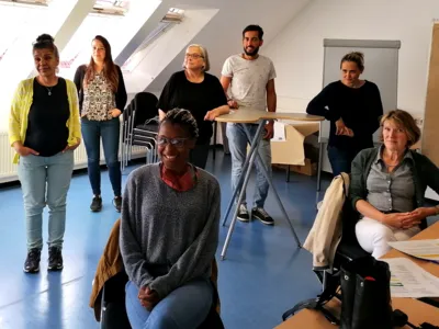 Sieben Personen - sechs Frauen und ein Mann - sitzen und stehen in einem Raum und blicken nach vorn.