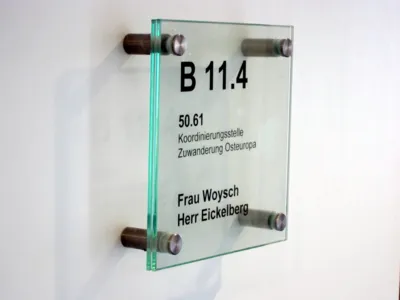 Foto eines transparenten B&uuml;roschildes, auf dem steht "Koordinierungsstelle Zuwanderung Osteuropa und die Namen "Frau Woysch" und "Herr Eickelberg".