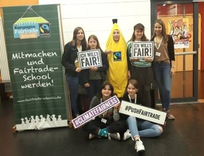 Schüler*innen mit Schildern zum Fairen Handel und in einem Bananenkostüm. Daneben ein Aufsteller zur Fairtrade Schools Kampagne.