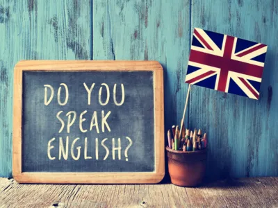Tafel, auf der mit Kreide geschrieben steht: " Do you speak english?, daneben ein Krug mit Stiften und einer britischen Fahne.