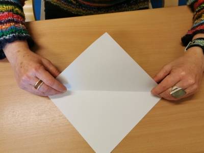 Eine Person faltet ein Blatt Papier zu einem Dreieck. 