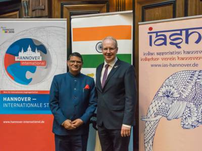 Oberbürgermeister Stefan Schostok und Generalkonsul Madan Lal Raigar stehen gemeinsam vor Roll-up-Plakaten, die auf Indien und Hannover International hinweisen.
