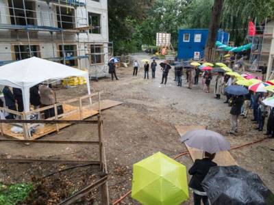 Menschen mit bunten Regenschirmen stehen auf einer Baustelle.