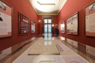 Langgstreckter Raum mit gerahmten Dokumenten an den Wänden und in einer Tischvitrine