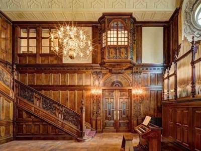 Halle mit getäfelten Wänden, hölzernem Treppenaufgang und Kronleuchter