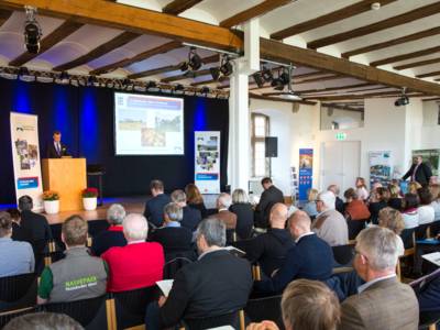 Publikum verfolgt einen Redner auf einer Bühne.