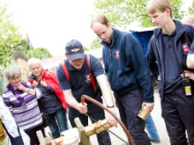 Ein Mann s&auml;gt Holz, weitere Menschen schauen zu.