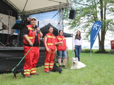 Vier Menschen und drei Hunde stehen vor einer B&uuml;hne.