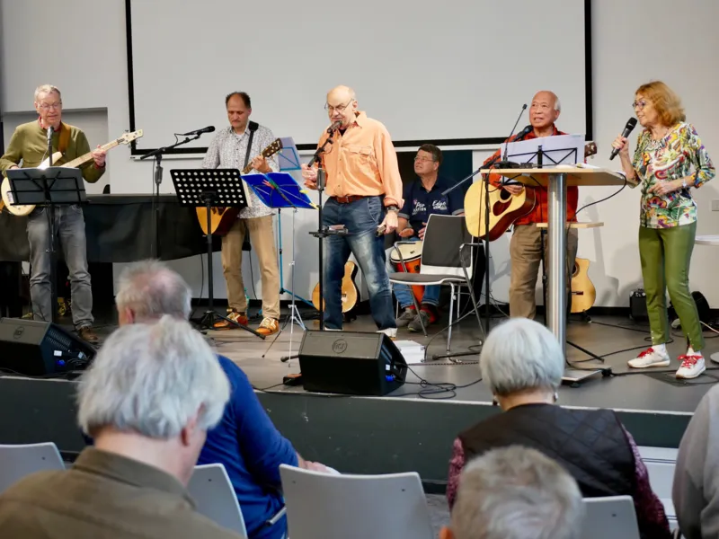 Sechs Personen auf einer B&uuml;hne mit Gitarren, Bass, Schlagzeug und Mikrofonen.