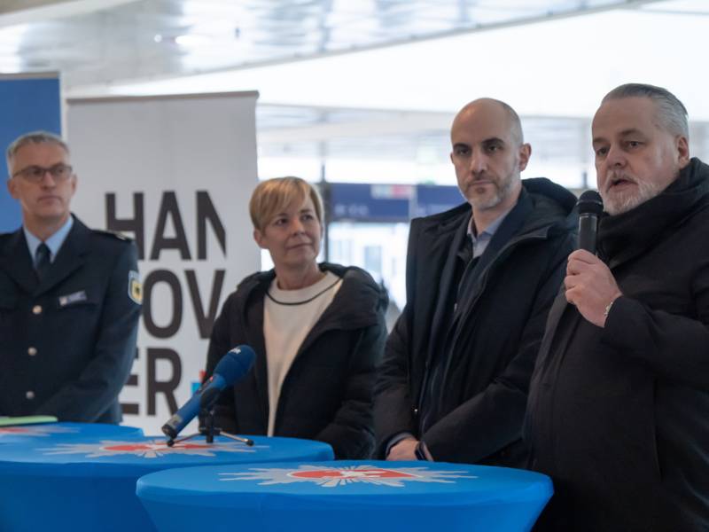 Vier Personen stehen hinter Stehtischen, eine von ihnen hält ein Mikrofon.