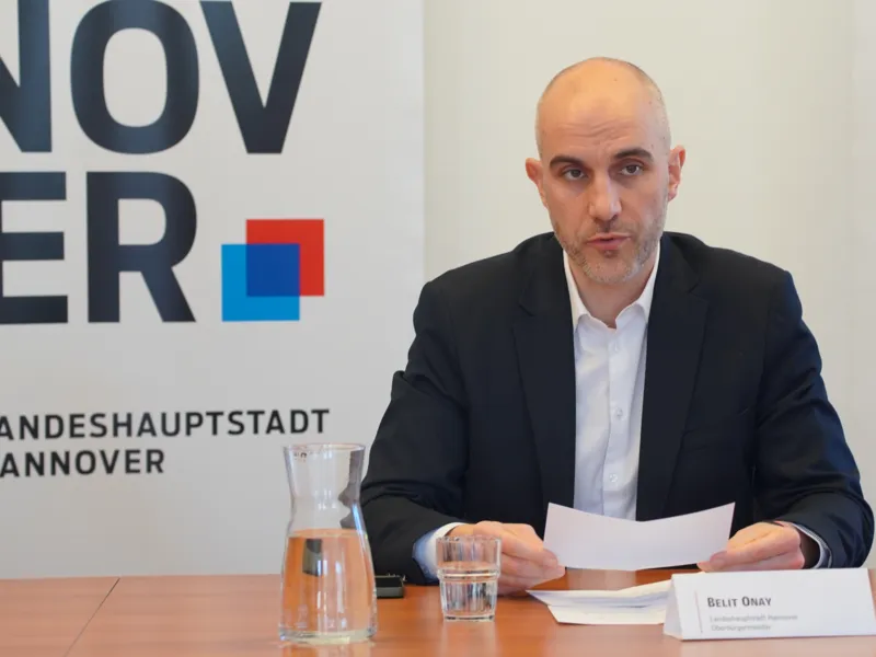 Ein Mann sitzt an einem Tisch, h&auml;lt ein Papier in den H&auml;nden und spricht.