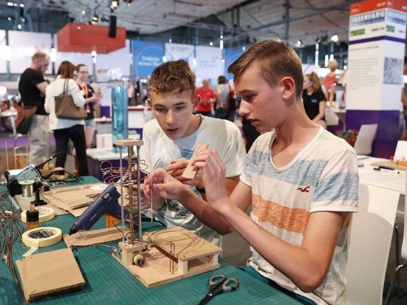 Zwei m&auml;nnliche Teenager an einem Tisch mit Werkzeug und einer Konstruktion aus Holz und Metall