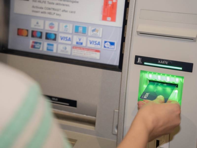 Eine Hand hält eine Visakarte, die sie in den Schlitz eines Bankautomaten führt.