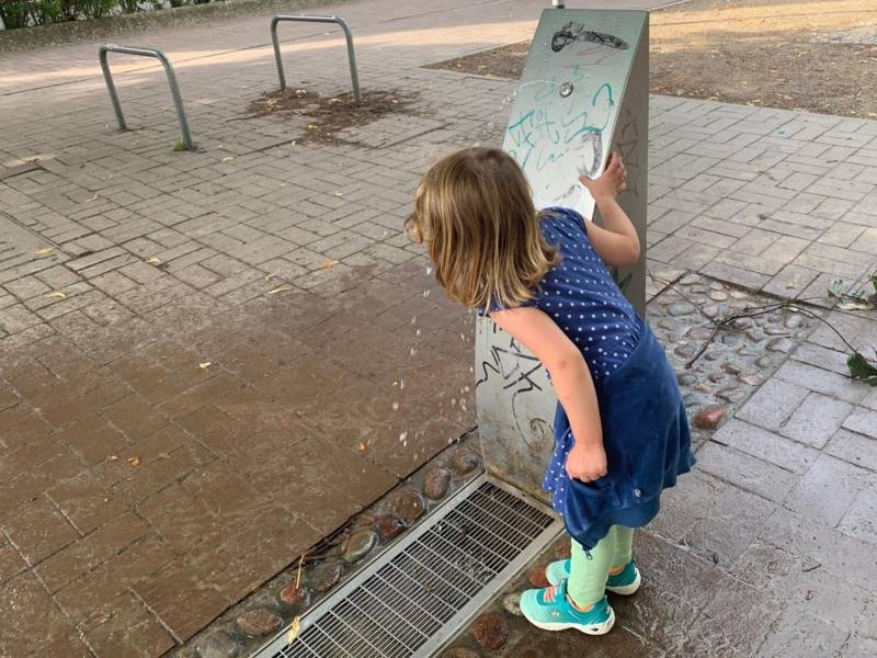 Ein M&auml;dchen, das an einem Brunnen steht.