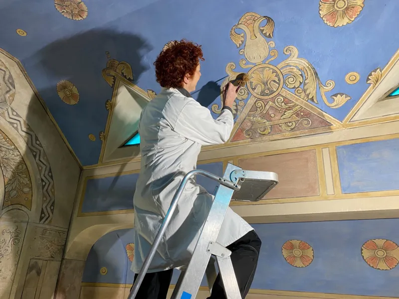 Eine Person, die Restaurationsarbeiten an einer Wand vornimmt.