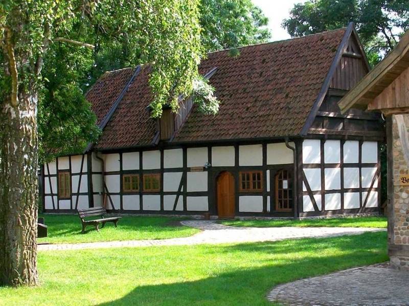 Restauriertes Fachwerkhaus, davor Rasen mit Bank, ein Weg und ein Baum