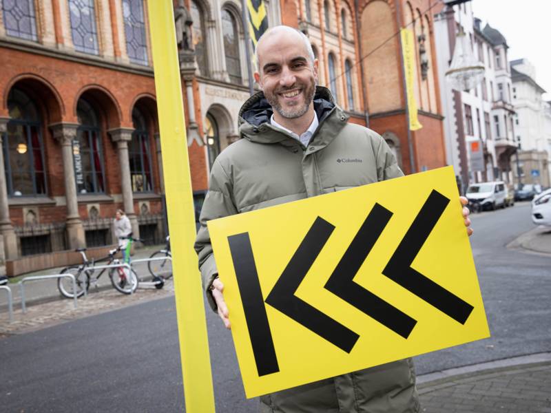 Ein lächelnder Mann mit einem schwarz-gelben Schild.