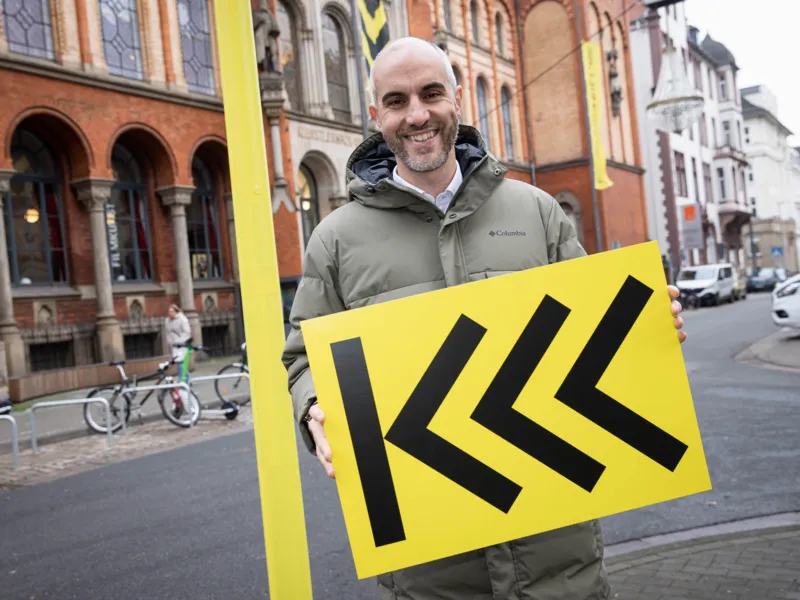 Ein l&auml;chelnder Mann mit einem schwarz-gelben Schild.