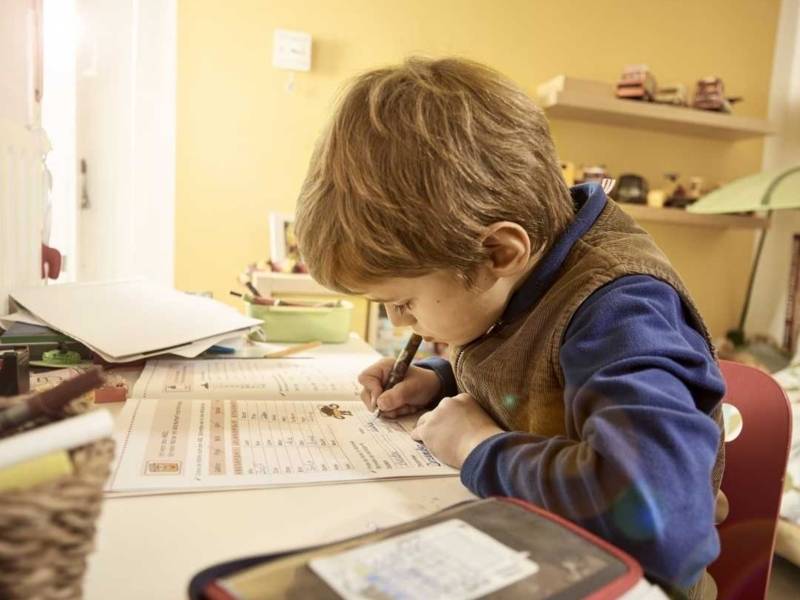 Ein Junge an einem Tisch schreibt in ein Aufgabenheft