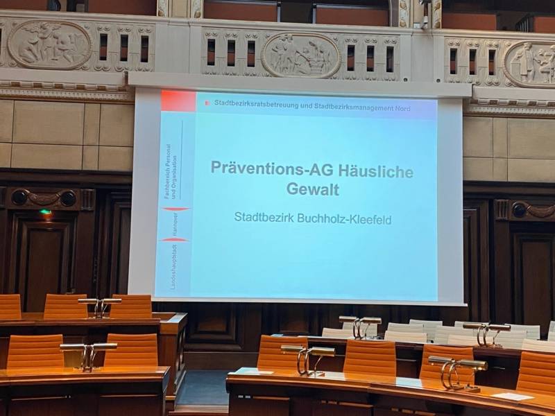 Podium mit großer Leinwand, auf der "Präventions-AG Häusliche Gewalt Stadtbezirk Buchholz-Kleefeld" steht