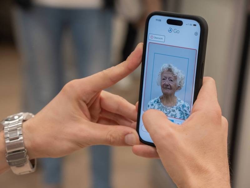 Eine Person h&auml;lt ein Handy in der Hand. &Uuml;ber die Handykamera ist eine zweite Person erkennbar, die in die Frontkamera schaut.