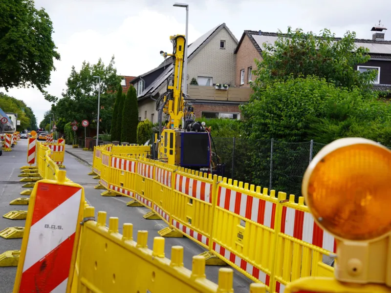 Rot-wei&szlig; gestreifte Markierungen und gelbe Absperrungen mit einer gelben Lamp links, dahinter eine Stra&szlig;e und Wohnh&auml;user.