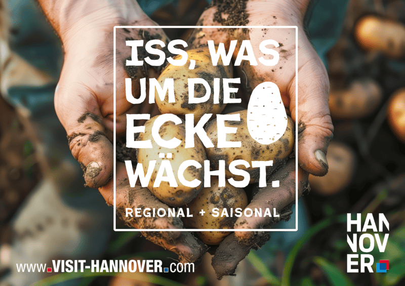 Motiv einer Postkarte. Mittendrin steht "Iss, was um die Ecke w&auml;chst". Im Hintergrund zwei H&auml;nde mit Kartoffeln.