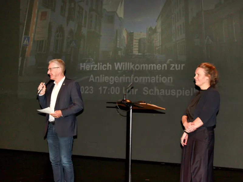 Ein Mann spricht in ein Mikrofon, eine Frau steht daneben.