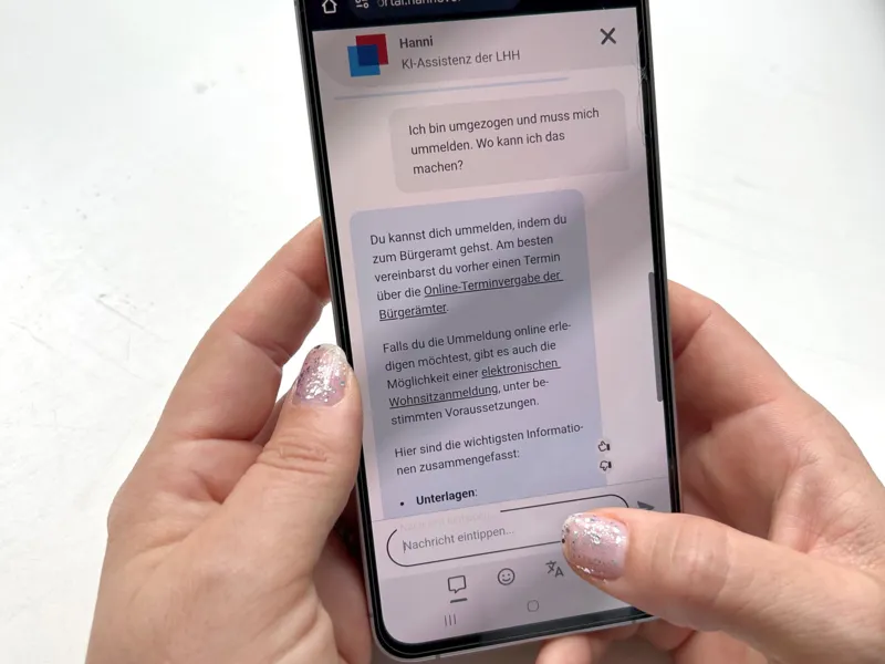 Zwei H&auml;nde halten ein Handy in der Hand. Auf dem Bildschirm ist "Hanni", der Chatbot der LHH ge&ouml;ffnet.