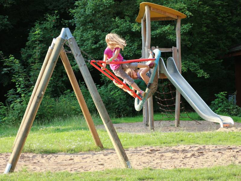 Kinder, die auf der Nestschaukel spielen. Eine Rutsche im Hintergrund.