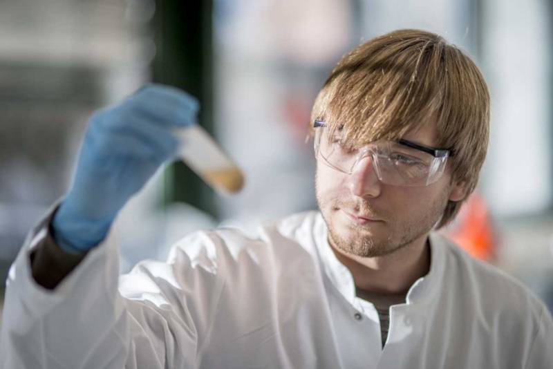 Mann mit Kittel und Schutzbrille h&auml;lt ein Reagenzglas in der Hand