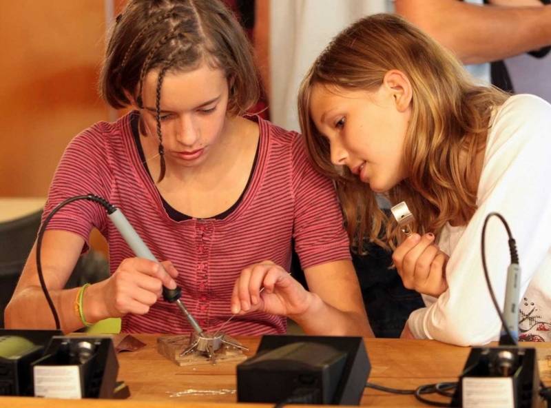 Zwei junge Frauen an einem Tisch mit Ger&auml;ten, die eine arbeitet mit einem L&ouml;tkolben