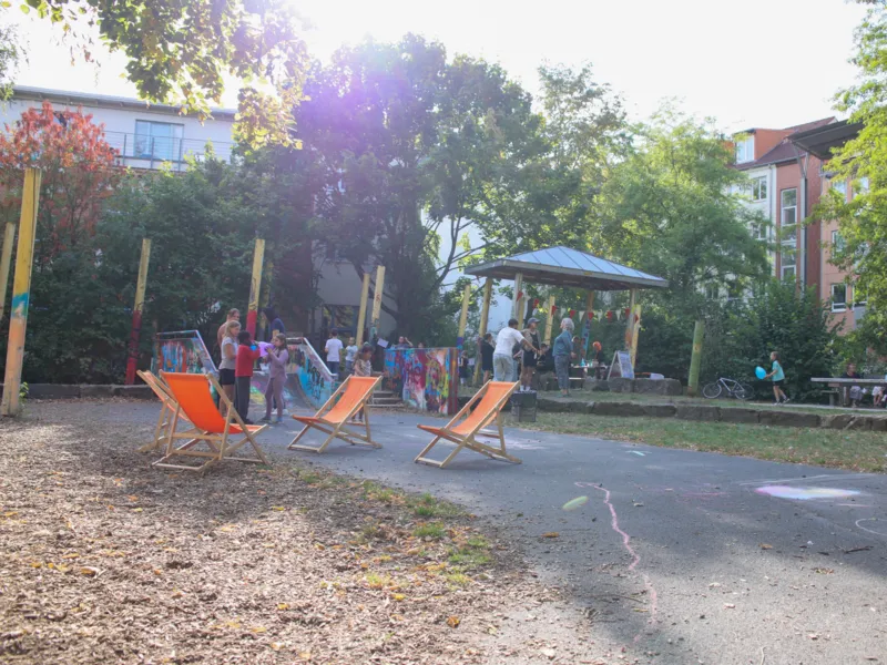 Blick auf einen Platz. Im Hintergrund Menschen, Liegesst&uuml;hle und Pavillons.