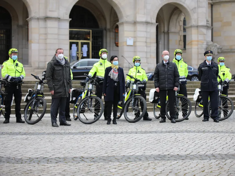 Zehn Personen, darunter einige mit Fahrrad, mit Maske und Abstand vor dem Neuen Rathaus