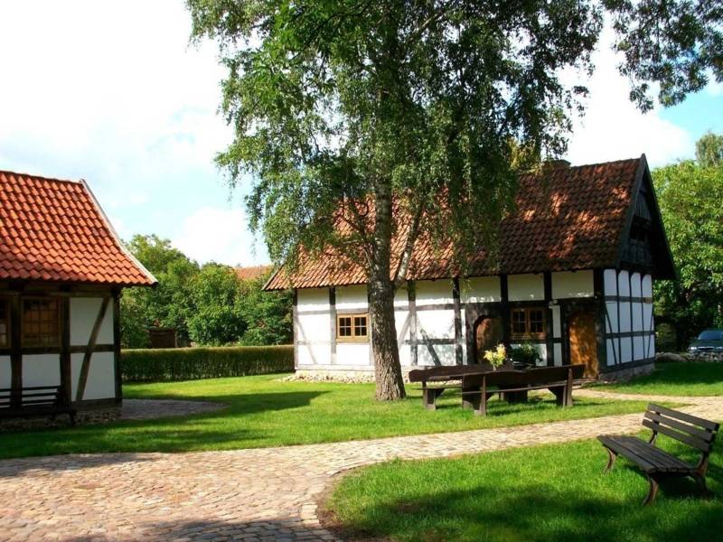 Zwei restaurierte Fachwerkh&auml;user, davor Rasen mit Baum und B&auml;nken und ein Weg