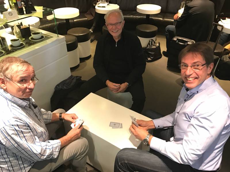 Drei Männer sitzen an einem Tisch und spielen ein Kartenspiel.