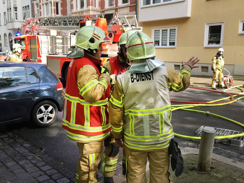 Im Vordergrund mehrere Einsatzkräfte der Feuerwehr Hannover, im Hintergrund eine Drehleiter vor der betroffenen Wohnung.
