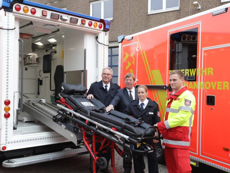 Feuerwehrchef Claus Lange, Feuerwehrdezernent Harald Härke, Schulleiterin Jeanette Mirande und Notfallsanitäter Andre Schmidt zeigen die automatische Einzughilfe für Fahrtragen an den neuen Rettungswagen.