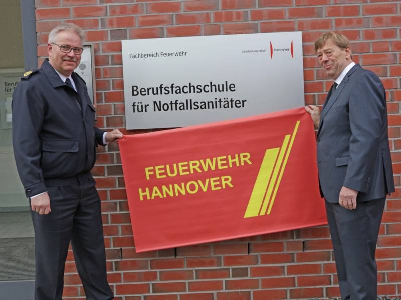 Feuerwehrdezernent Harald Härke und der Direktor der Feuerwehr Claus Lange enthüllen das neue Schild an der Berufsfachschule.