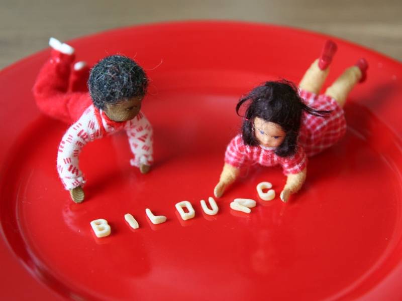 Bildungshungrig: zwei Puppen mit Buchstabennudeln auf einem Teller