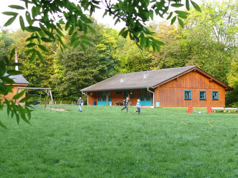 Holzhaus auf grüner Wiese mit spielenden Kindern