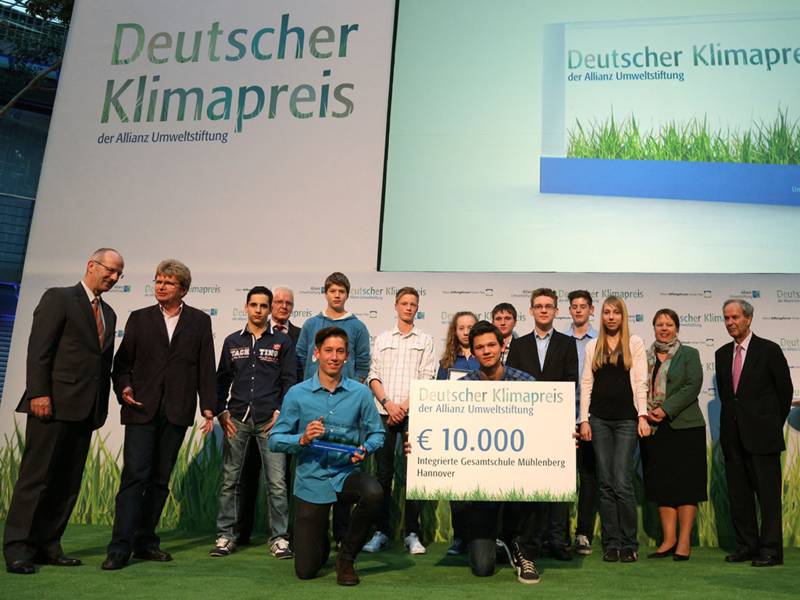 Eine Bühne, auf der mehr als ein dutzend vor allem junge Personen stehen, zwei von ihnen halten die Auszeichnung mit dem "Deutschen Klimapreis" in den Händen
