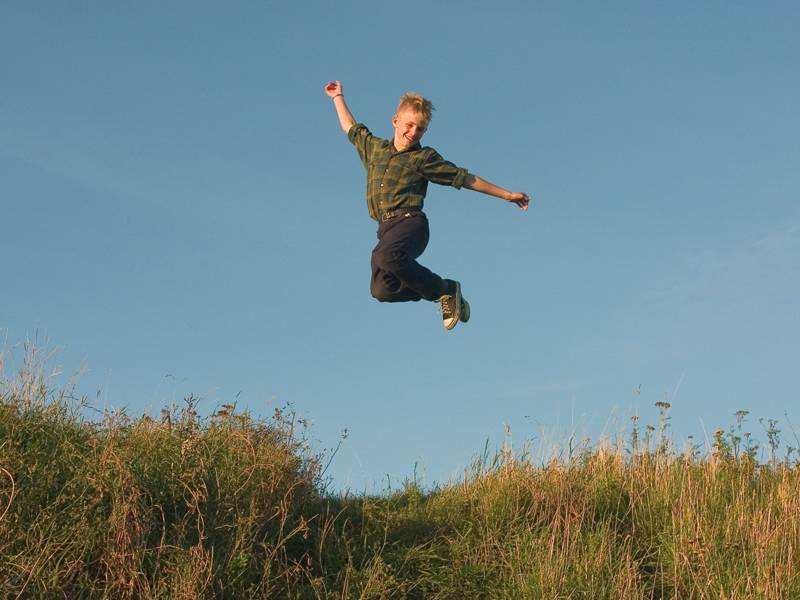 Ein Junge springt über einer grünen Wiese in die Luft.
