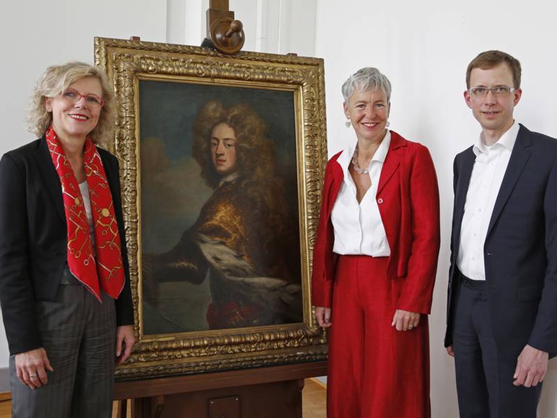 Drei Menschen stehen neben einem Gemälde.