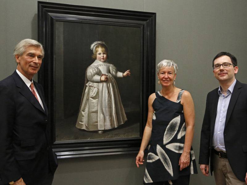 Zwei Männer und eine Frau stehen vor einem Gemälde.