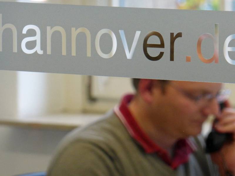 Schriftzug "Hannover.de" auf einer Glasscheibe, im Hintergrund sitzt ein Mann.